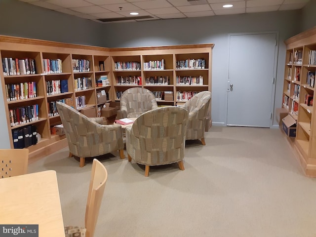 living area featuring recessed lighting, wall of books, a paneled ceiling, and light colored carpet