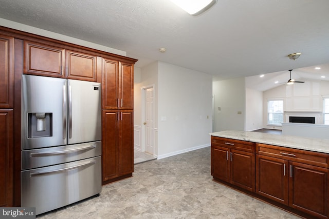 kitchen featuring a ceiling fan, stainless steel fridge with ice dispenser, light stone countertops, vaulted ceiling, and a fireplace