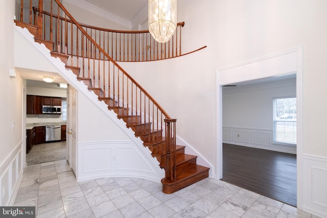 stairs with crown molding, marble finish floor, a chandelier, and a decorative wall