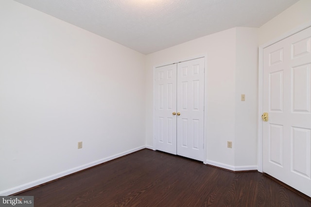 unfurnished bedroom featuring dark wood-type flooring, a closet, and baseboards