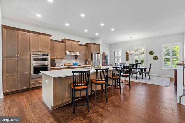 kitchen with a kitchen island with sink, stainless steel appliances, decorative backsplash, a kitchen bar, and decorative light fixtures