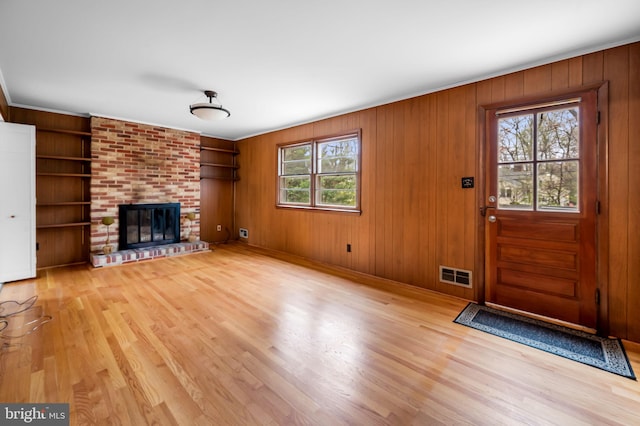 unfurnished living room with visible vents, wood walls, a brick fireplace, light wood finished floors, and built in shelves