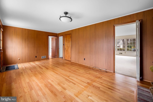 unfurnished room with wooden walls, visible vents, ornamental molding, and light wood-style flooring