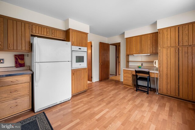 kitchen featuring light countertops, brown cabinetry, white appliances, and light wood-style floors