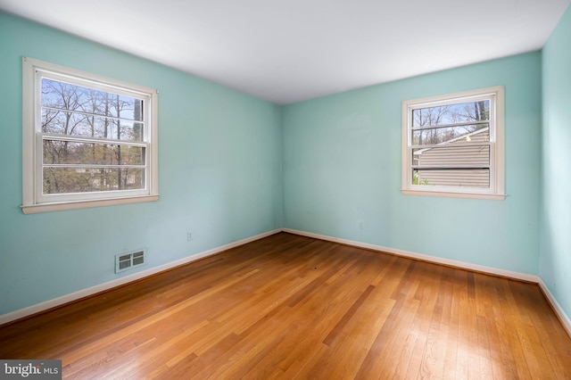 unfurnished room featuring baseboards, visible vents, and hardwood / wood-style flooring