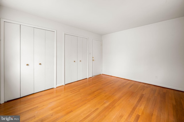 unfurnished bedroom featuring two closets and light wood-style floors