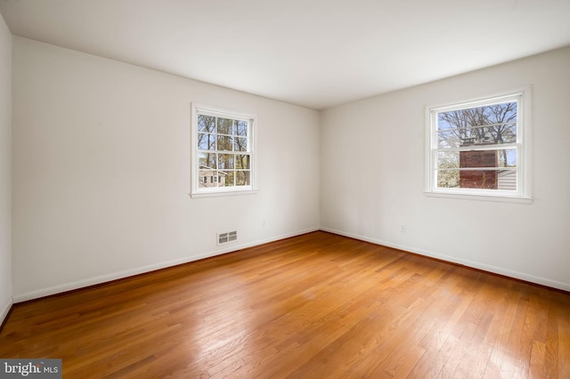 unfurnished room featuring light wood-style floors, visible vents, and baseboards