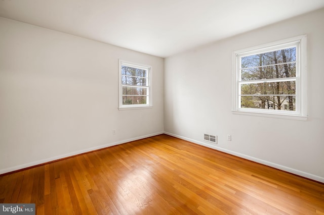 empty room featuring light wood finished floors, baseboards, and visible vents