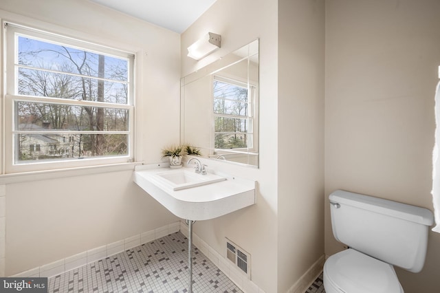 half bathroom featuring baseboards, tile patterned floors, toilet, visible vents, and a sink