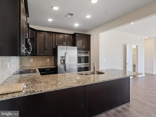 kitchen with sink, light stone counters, appliances with stainless steel finishes, kitchen peninsula, and decorative backsplash