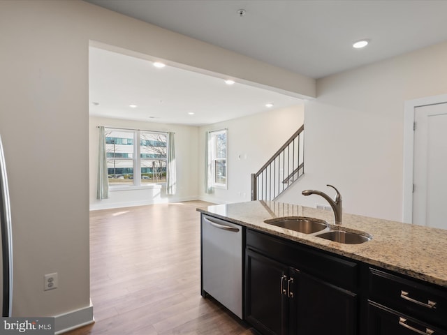 kitchen with light stone counters, stainless steel dishwasher, sink, and light hardwood / wood-style flooring