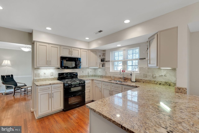 kitchen featuring visible vents, light stone counters, black appliances, open shelves, and a sink