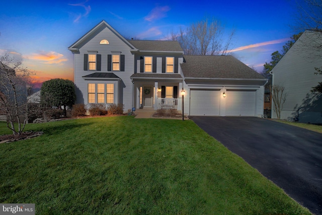 view of front of property featuring an attached garage, covered porch, aphalt driveway, and a lawn