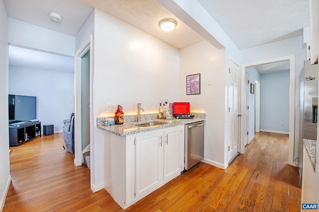 kitchen with sink, white cabinetry, appliances with stainless steel finishes, light stone countertops, and light hardwood / wood-style floors