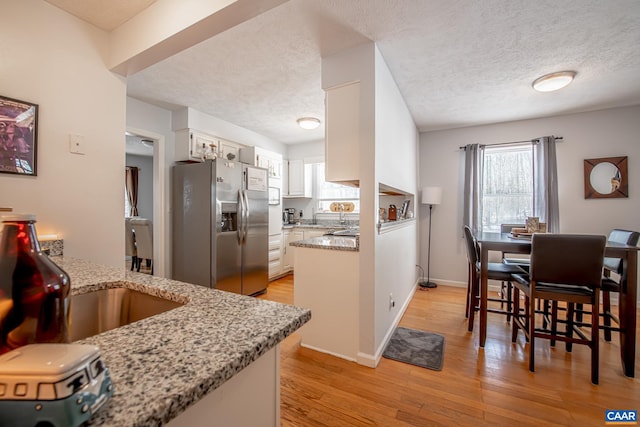 kitchen with white cabinets, light stone counters, kitchen peninsula, stainless steel refrigerator with ice dispenser, and light wood-type flooring