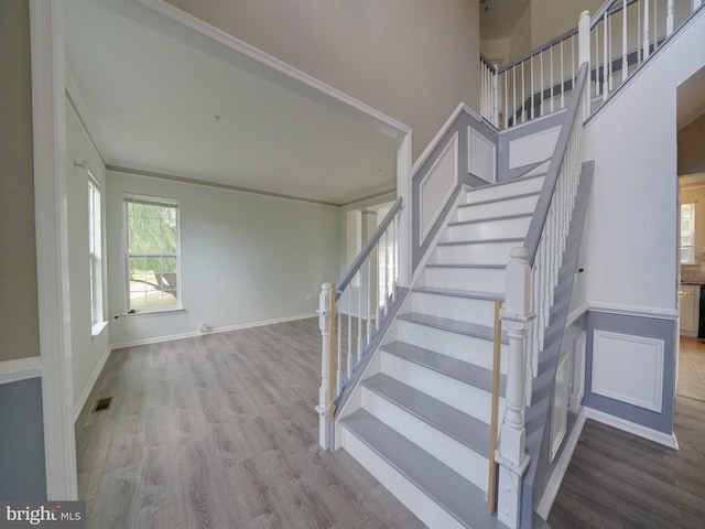 staircase featuring a high ceiling, wood finished floors, visible vents, and baseboards