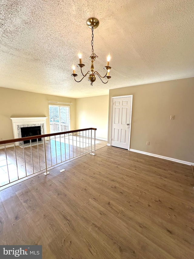 spare room featuring wood-type flooring, a premium fireplace, a chandelier, and a textured ceiling