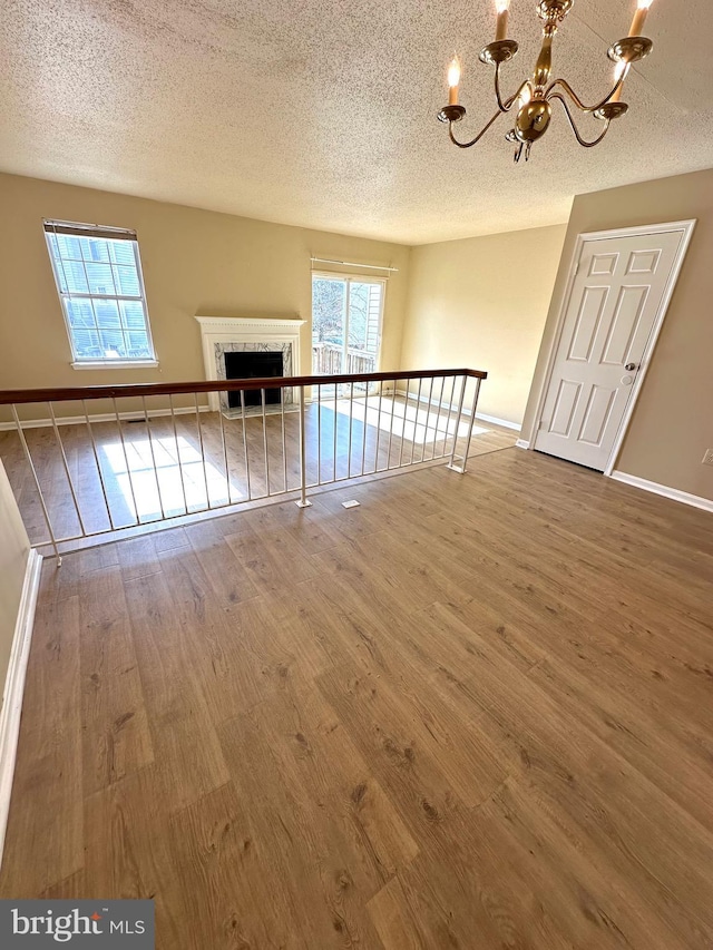 unfurnished living room with an inviting chandelier, a healthy amount of sunlight, wood-type flooring, and a textured ceiling