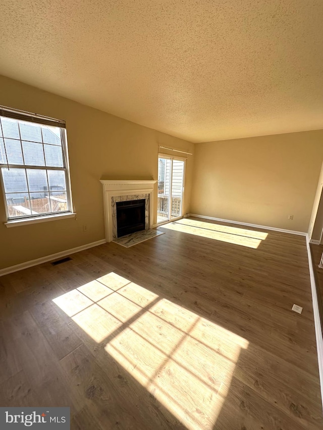 unfurnished living room with hardwood / wood-style flooring, a high end fireplace, and a textured ceiling