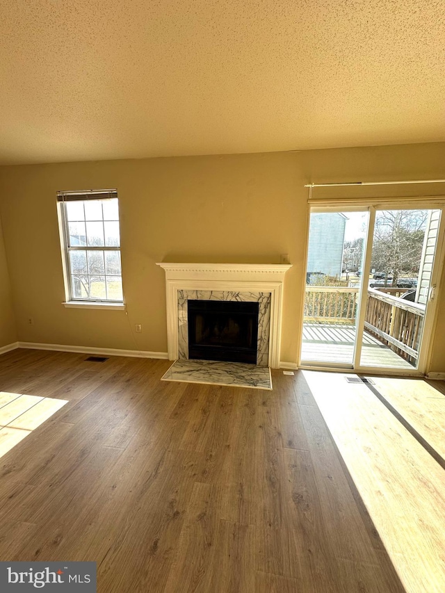 unfurnished living room featuring hardwood / wood-style flooring, a high end fireplace, and a healthy amount of sunlight