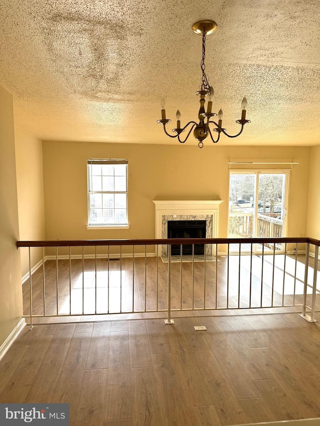 unfurnished living room featuring hardwood / wood-style floors, a notable chandelier, a high end fireplace, and a healthy amount of sunlight