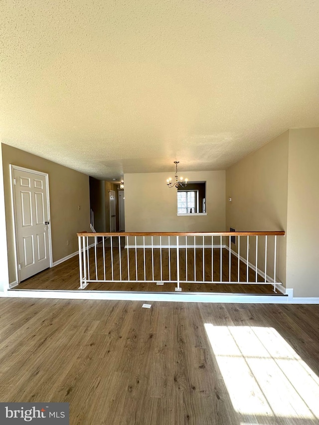 unfurnished room featuring a notable chandelier, hardwood / wood-style floors, and a textured ceiling