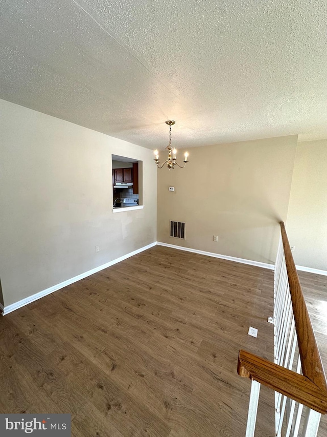 unfurnished room with dark hardwood / wood-style floors, a textured ceiling, and an inviting chandelier