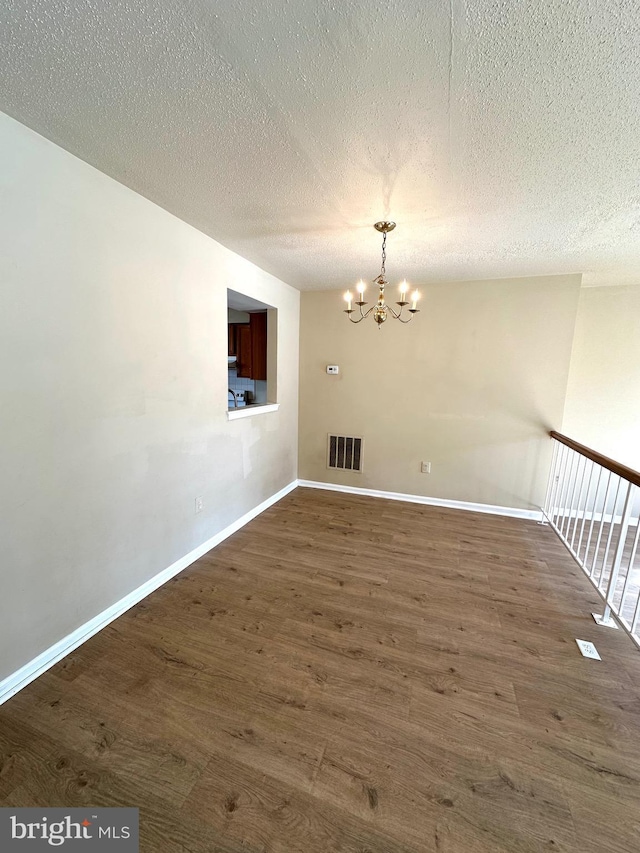 spare room featuring dark wood-type flooring, a textured ceiling, and an inviting chandelier