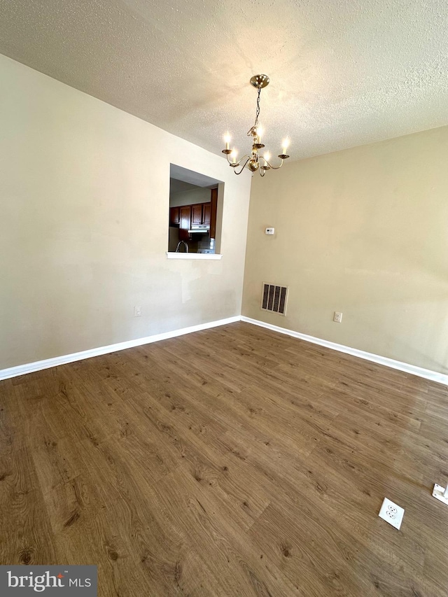 unfurnished dining area featuring a notable chandelier, dark hardwood / wood-style floors, and a textured ceiling