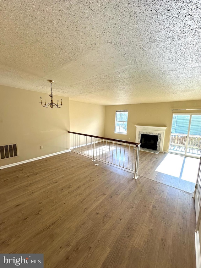 unfurnished living room with an inviting chandelier, wood-type flooring, a high end fireplace, and a textured ceiling