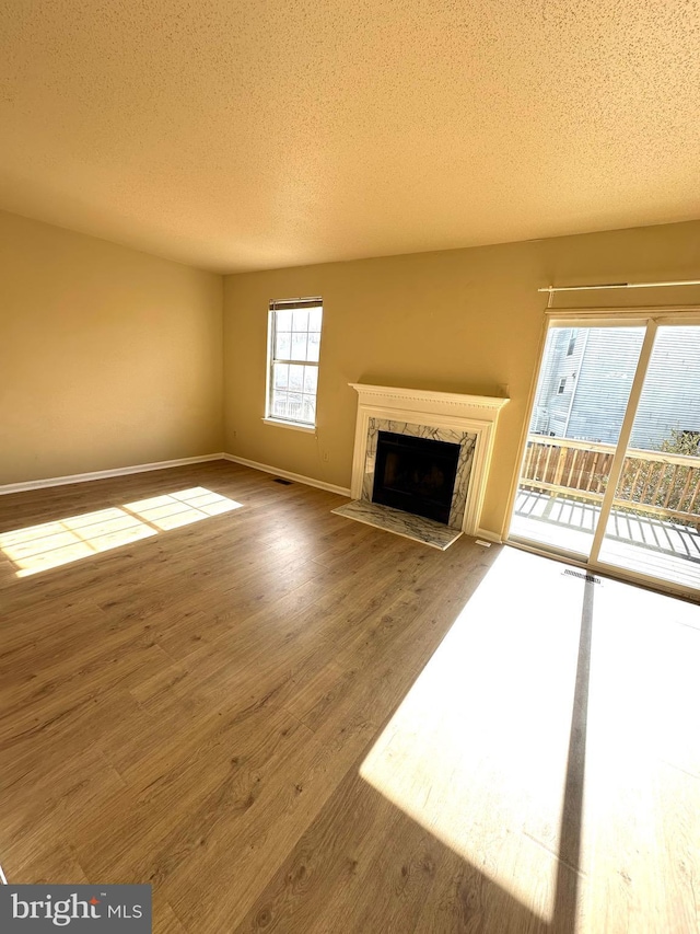 unfurnished living room with hardwood / wood-style flooring, a high end fireplace, and a textured ceiling