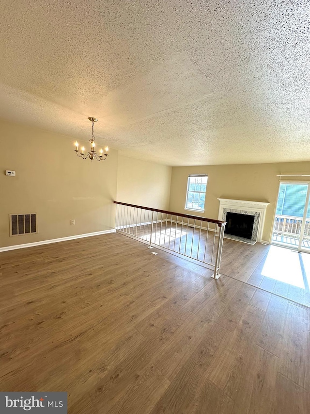 unfurnished living room with hardwood / wood-style flooring, a textured ceiling, a chandelier, and a fireplace