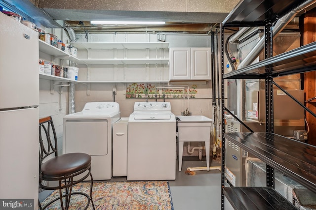 clothes washing area featuring concrete block wall, cabinet space, and washing machine and clothes dryer