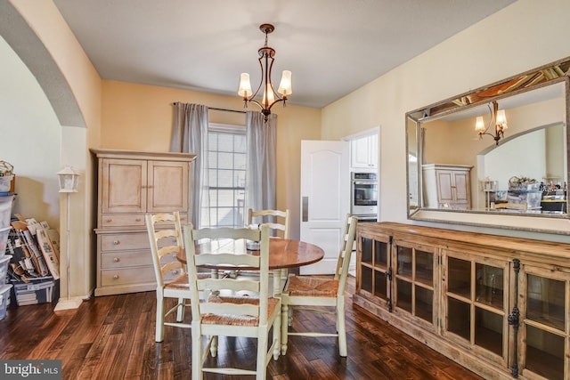 dining area with dark wood-style floors, arched walkways, and an inviting chandelier