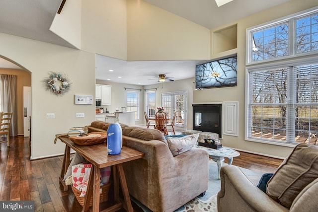 living room featuring a towering ceiling, baseboards, arched walkways, and dark wood-type flooring