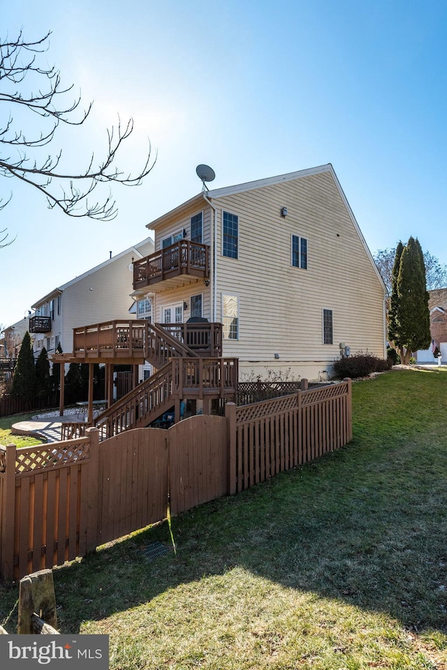 rear view of house with fence, a balcony, and a lawn