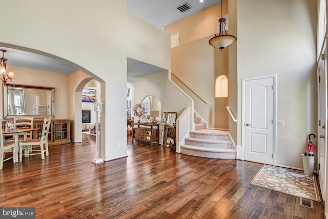 foyer entrance with dark wood-style floors, visible vents, a high ceiling, and stairs