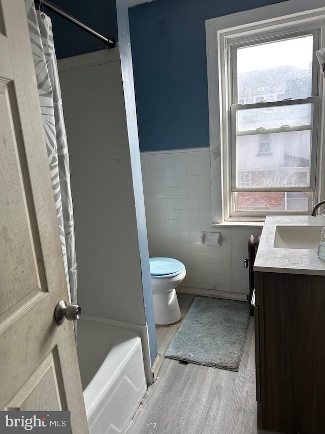 bathroom featuring wood-type flooring, tile walls, vanity, and toilet