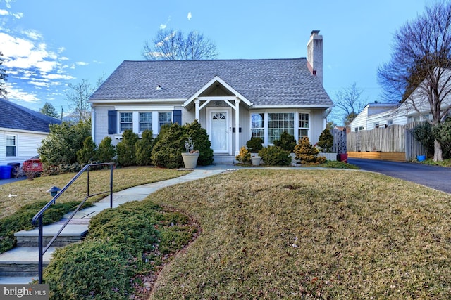 view of front of home with a shingled roof, a chimney, a front yard, and fence