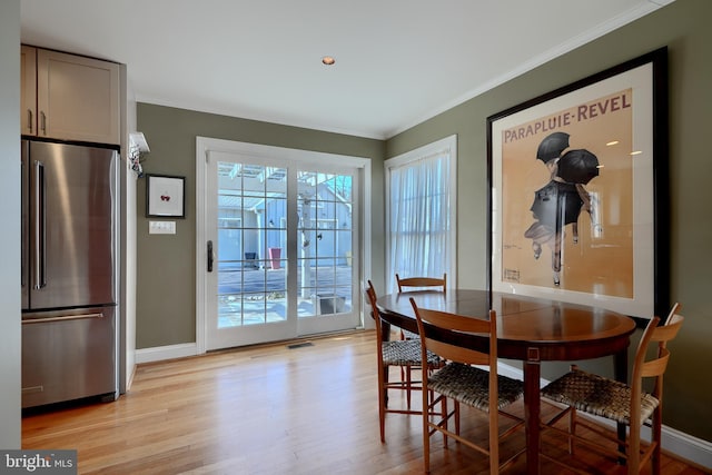 dining space with light wood finished floors, ornamental molding, visible vents, and baseboards