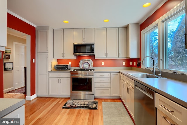 kitchen with stainless steel appliances, light countertops, light wood-style flooring, white cabinetry, and a sink