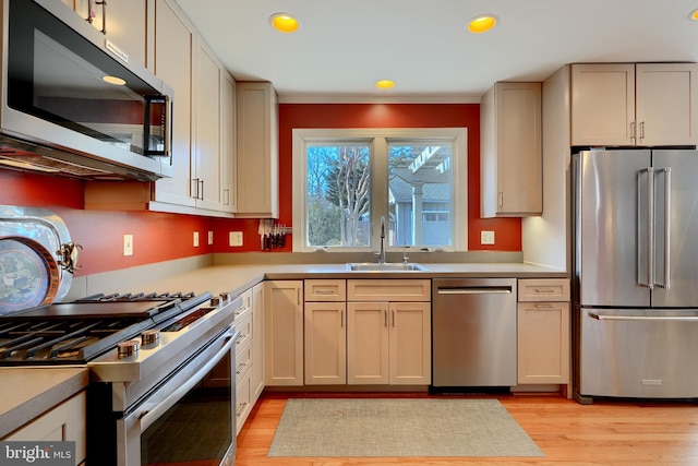 kitchen with light wood finished floors, stainless steel appliances, light countertops, cream cabinets, and a sink