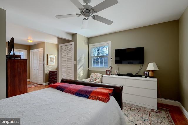 bedroom with light wood-type flooring, two closets, a ceiling fan, and baseboards