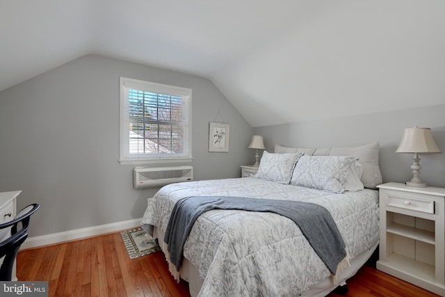 bedroom with lofted ceiling, a wall unit AC, baseboards, and wood finished floors