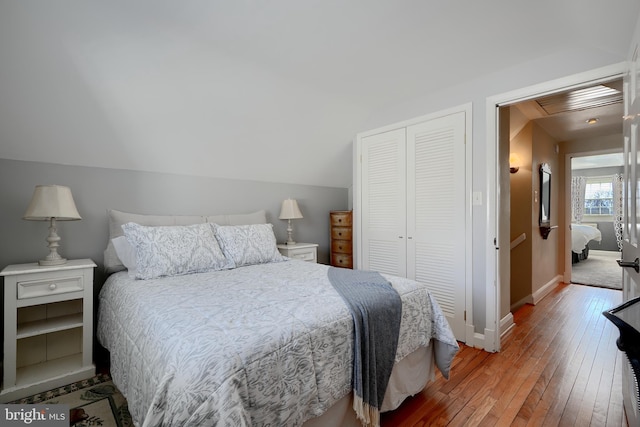 bedroom featuring lofted ceiling, baseboards, a closet, and wood finished floors