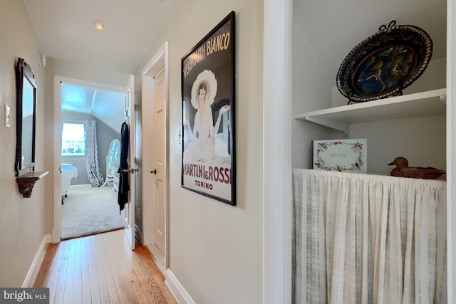 corridor with light wood finished floors, baseboards, and vaulted ceiling