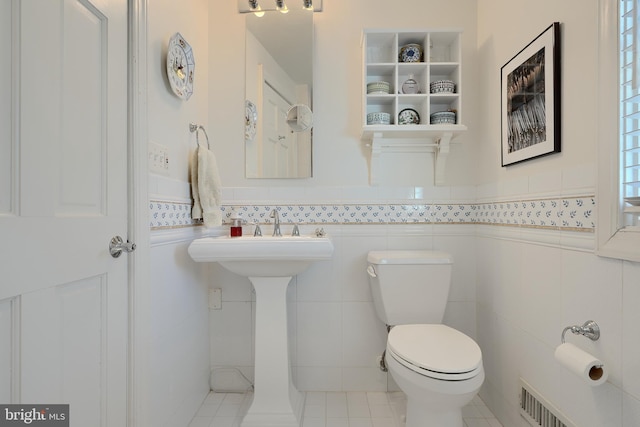 half bath with toilet, visible vents, tile walls, and wainscoting