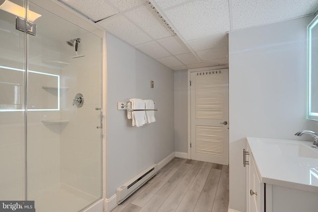 bathroom with baseboard heating, a stall shower, vanity, wood finished floors, and a drop ceiling