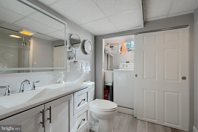 bathroom featuring washer / dryer, toilet, wood finished floors, vanity, and a paneled ceiling