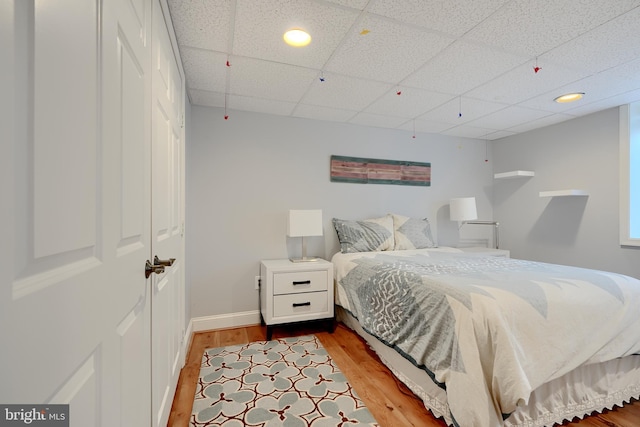 bedroom with baseboards, a drop ceiling, and light wood-style floors